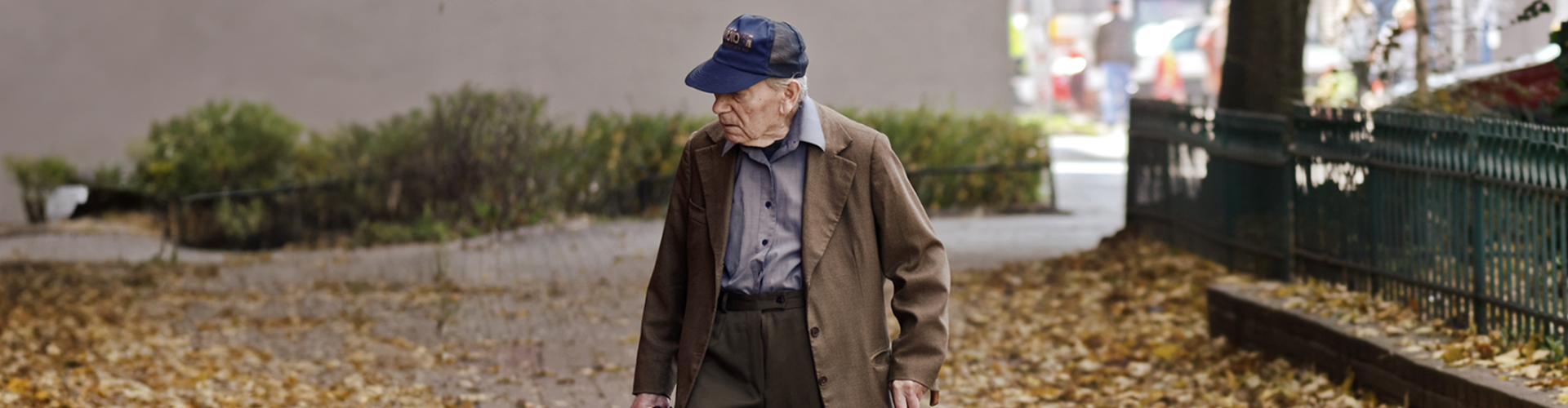 An elderly man walking in a street full of fallen leaves.